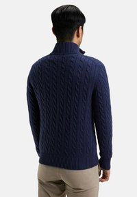 Pull en laine bleu marine à mailles torsadées avec un col montant, des poignets et un ourlet côtelés. Présente un motif texturé sur l'ensemble du tissu.