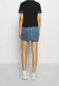 Svart kortärmad t-shirt med vita accentsträck, parat med en ljusblå denim minikjol med fransad nederkant och två bakfickor.