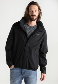 Veste légère noire avec capuche, dotée d'une fermeture éclair à l'avant, de poignets élastiques et d'un bas ajusté. Le matériau semble lisse et résistant à l'eau.