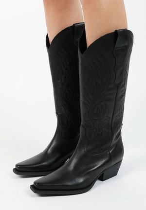 Zwarte leren cowboylaarzen met puntige neuzen, gegraveerde patronen en lage blokhakken. Voorzien van lange schachten met een lichte scalloping aan de bovenkant.