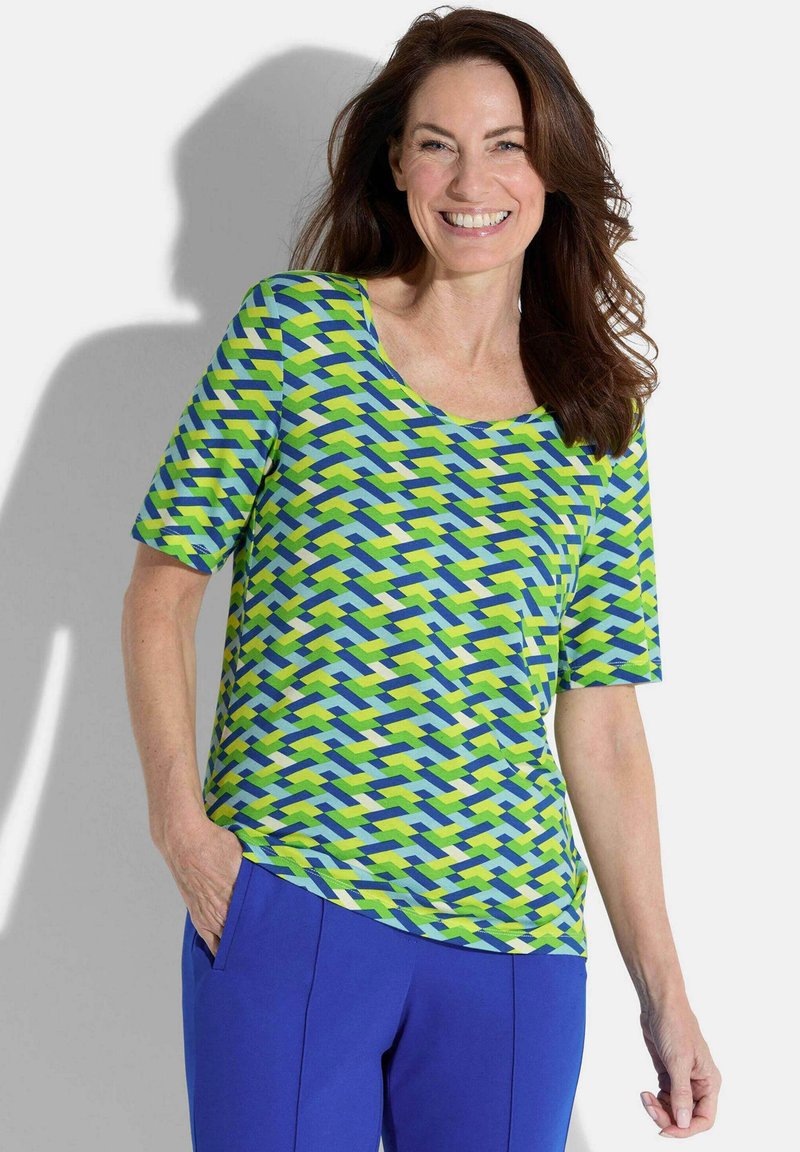 Haut à manches courtes dans un motif géométrique vert, bleu et blanc ; tissu doux, encolure ronde, coupe décontractée, associé à un pantalon bleu.