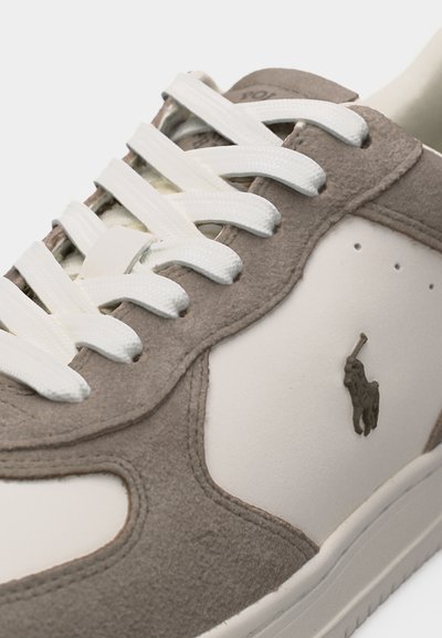 Κοντινό πλάνο μπεζ και ανοιχτό καφέ αθλητικού παπουτσιού με λευκά κορδόνια και σκούρο καφέ λογότυπο παίκτη πόλο στο πλαϊνό πάνελ.