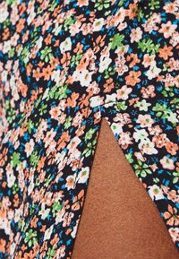 Blommig tyg i svart med små orange, gröna och vita blommor. Har en sidoklyvning med en ren söm. Slät textur.