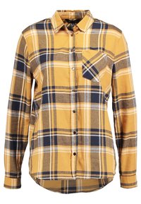 Camicia a maniche lunghe a scacchi gialla, blu navy e bianca, con colletto e taschino sul petto, orlo leggermente curvato.