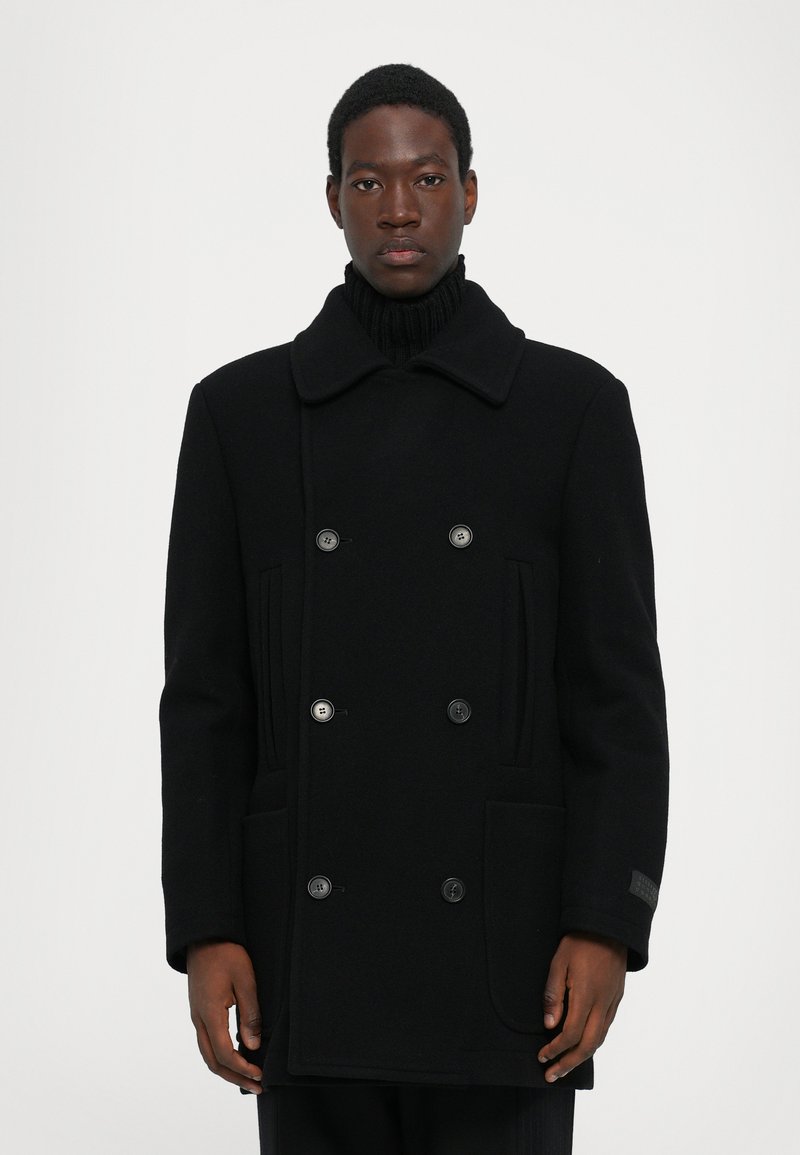 Svart ylle peacoat med dubbelknäppt design, stor krage och två framfickor. Har sex matchande knappar och ribbad halsringning.