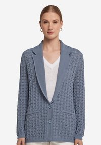 Ljusblå stickad cardigan med sjalkrage, två knappar och intrikata mönster. Har fickor och ribbade ärmslut.