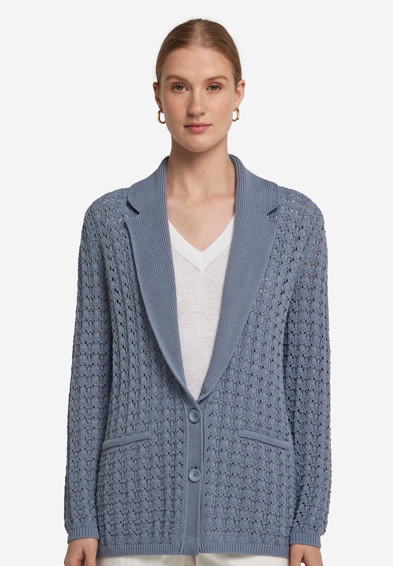 Ljusblå stickad cardigan med sjalkrage, två knappar och intrikata mönster. Har fickor och ribbade ärmslut.