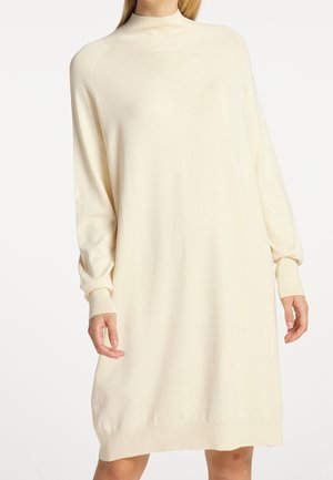Abito lavorato a maglia color crema con colletto alto, maniche lunghe e polsini a coste, caratterizzato da una vestibilità ampia e orlo leggermente affusolato.