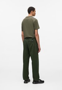 Camiseta de algodón verde oliva con cuello redondo, combinada con pantalones de pierna ancha verde oscuro con un bolsillo trasero y parche de la marca. Zapatillas negras.