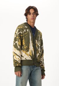 Grønn og kremfarget strikket cardigan med abstrakt mønster, med V-hals, fulle knapper foran og ribbestrikkede mansjetter og kant.