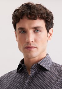 Camicia da uomo navy con motivo geometrico di piccoli cerchi, colletto a bottoni e tessuto testurizzato. Inquadratura ravvicinata della parte superiore del corpo.