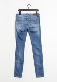 Jeans ajustados en denim azul claro, con una cintura de talle medio, una parche de cuero marrón en la parte posterior y dos bolsillos traseros con detalles de costura.