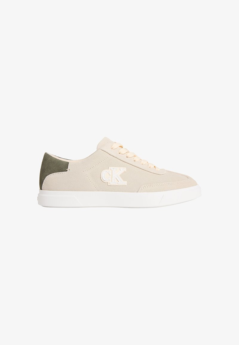 Baskets basses en daim beige avec semelle blanche, lacets beiges, patch talon vert olive et logo "cK" blanc sur le côté.