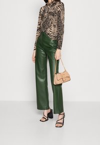 Groene leren wijde broek, lange mouwen top met dierenprint, beige handtas met een ketting en zwarte strappy hakken. Gladde texturen en contrasterende kleuren.