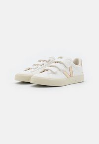 Zapatillas blancas con acentos en marrón, hechas de cuero, con correas de Velcro, punta redonda y suelas de goma texturizada. Diseño limpio y minimalista.