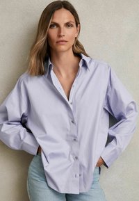 Light purple button-up shirt with a classic collar, single chest pocket, and long, slightly puffed sleeves. Smooth texture, casual fit.