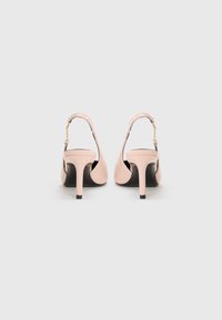 Tacchi slingback in pelle rosa pallido con design affusolato, tacco sottile e suola nera. Presentano una cintura regolabile in metallo dorato.
