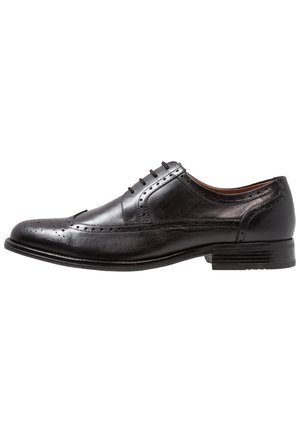Chaussure Oxford pour homme en cuir noir avec détails brogue, laçage fermé et petit talon empilé, vue de côté sur fond blanc.