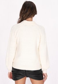 Maglione bianco in maglia a trama con collo alto e maniche raglan, caratterizzato da un orlo a coste e un tessuto morbido e peloso.