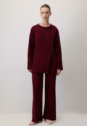 Burgundy ribbed knit sweater with long sleeves and side buttons, paired with matching wide-leg pants, textured fabric, and soft finish.
