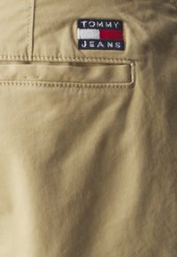 Béžová tkanina se zadní kapsou a nášivkou "TOMMY JEANS" v námořnické, červené a bílé barvě, s obdélníkovým designem.