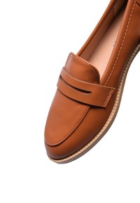 Mocassino in pelle marrone con texture liscia, punta arrotondata e una fascia decorativa. Presenta una suola di colore chiaro e texture.