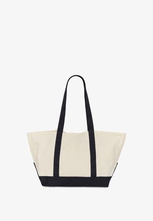 Beige canvas tas met zwarte handvatten en zwarte bodem, breed en ruim van formaat met lange schouderbanden voor gemakkelijk dragen.
