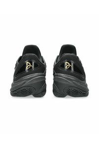 Scarpe da atletica nere con tomaia in rete, suola in gomma texturizzata e un emblema lucido sul tallone. Design moderno e snodato.