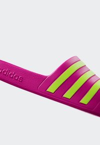 Pink slide sandal made of textured rubber, featuring three bold green stripes and embossed branding on the strap.