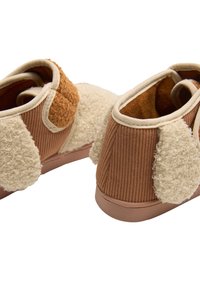 Zapatos de pana marrón con detalles en las orejas de color crema y peluche, y un forro interior suave. Diseño redondeado y suelas flexibles de goma.