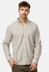 Lyse beige langærmet skjorte med knapfront, der har en subtil vertikal tekstur og en lille logo på brystet. Har knapmanchetter og krave.