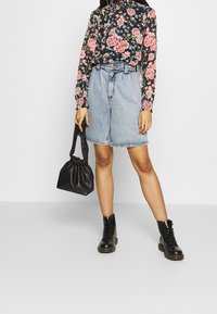 Blumenmuster Langarmbluse mit schwarzem Grund, hoher Kragen; hellblaue Jeansshorts mit tailliertem Bund; schwarze Bucket Bag; schwarze Schnürstiefel.