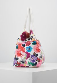 Květinová kabelka s bílým textilním povrchem, zdobená barevnými květy v různých odstínech růžové, fialové a modré. Má dvě bílé rukojeti.
