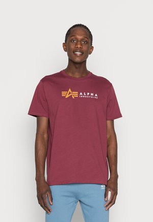 Maroon cotton t-shirt featuring a printed orange logo of "ALPHA INDUSTRIES" and a minimalist design with short sleeves and a crew neck.