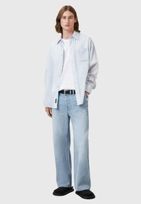 Camicia a righe azzurre chiare con bottoni, t-shirt bianca, jeans a gamba larga blu sbiaditi, cintura nera e scarpe slip-on nere.