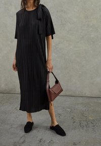 Schwarzes plissiertes Midikleid mit kurzen Ärmeln und einer seitlichen Schleifendetail, kombiniert mit schwarzen Mules und einer braunen strukturierten Handtasche.