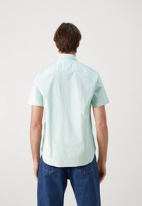 Camisa de manga corta en verde menta claro con cuello abotonado y sutiles rayas verticales, hecha de una tela ligera.