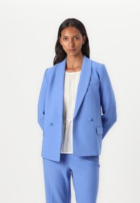 Light blue tailored blazer with a shawl collar, double button closure, and patch pockets, paired with a white textured blouse.
