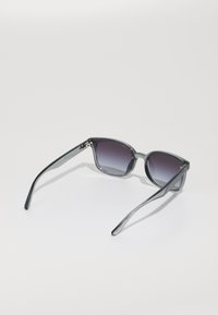 Ochelari de soare tip cat-eye cu un cadru transparent gri și lentile violet cu un gradient. Brațe elegante cu un detaliu subtil de branding.
