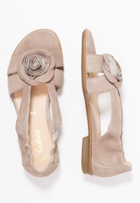 Beżowe zamszowe sandały na otwartym palcu z motywem róży, elastycznymi panelami bocznymi oraz niskim, solidnym obcasem dla wygody.