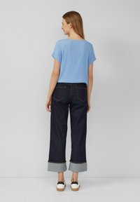 Lichtblauw, gestructureerd bovenstuk met korte mouwen, gecombineerd met donkerblauwe wijduitlopende jeans met opgerolde zoom en contrasterende stof. 