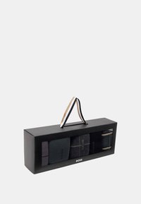 Geschenkbox mit vier Paar Socken in verschiedenen Schwarz- und Grautönen, mit einem Griff oben und einem transparenten Sichtfenster.