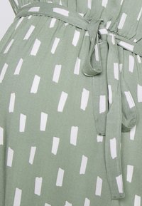 Zielona sukienka z wzorzystym deseniem, zawierającym białe prostokątne kształty. Wykonana z teksturowanej tkaniny, z paskiem do wiązania w talii.