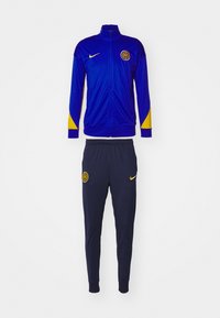 Completo da allenamento Nike composto da una giacca blu con dettagli gialli e logo, abbinata a pantaloni blu navy anch'essi con il logo. Leggero, vestibilità atletica.