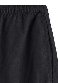 I pantaloni neri in lino presentano una vita elasticizzata, un tessuto leggermente testurizzato e tasche laterali. I dettagli delle cuciture sono visibili lungo le cuciture.