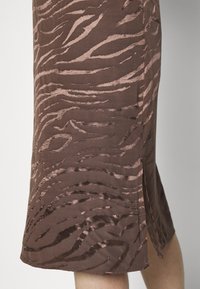 Saia castanha com um padrão subtil de riscas de zebra. Textura suave, até ao joelho, com uma fenda lateral para facilitar o movimento e acabamento liso.