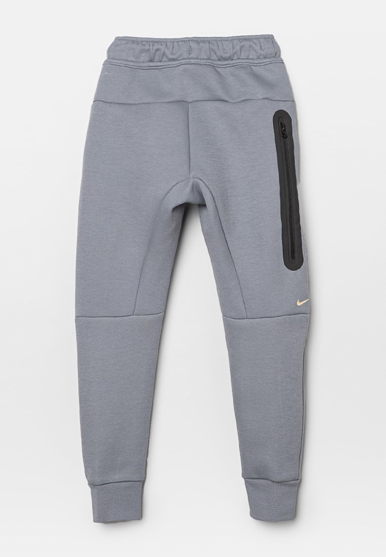 Pantaloni sportivi grigi con vestibilità attillata, vita elastica e una tasca con zip laterale nera. Tessuto morbido con polsini a costine. Logo Nike in oro.