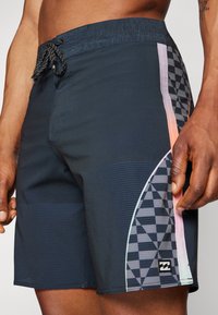 Boardshorts made of dark blue fabric features side accents with a checkerboard pattern and light gradient stripes in pink and aqua.