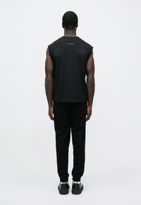 Fekete, ujjatlan felső kerek nyakkivágással, könnyű anyagból, fekete, szűk szárú nadrággal és fekete tornacipővel párosítva. Minimalista dizájn.