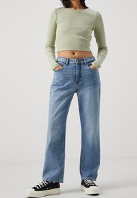 Světlé zelené dlouhé rukávy crop top spárované s modrými vysoce pasovými rovnými džínami a černými teniskami s bílými podrážkami.